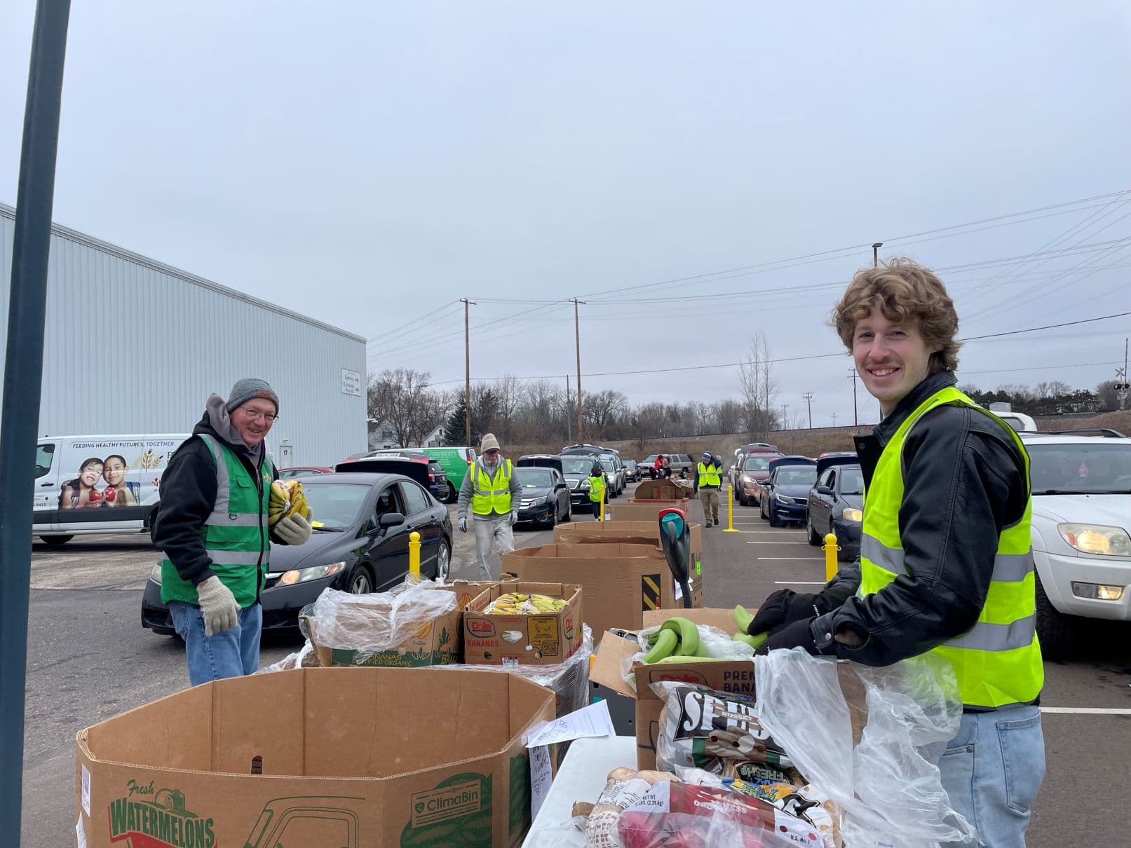 Two volunteers hand out food outside to people driving up to receive groceries at Feed My People Food Bank in Eau Claire.